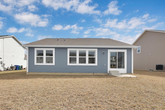 rear view of property featuring roof with shingles, central AC, and a yard