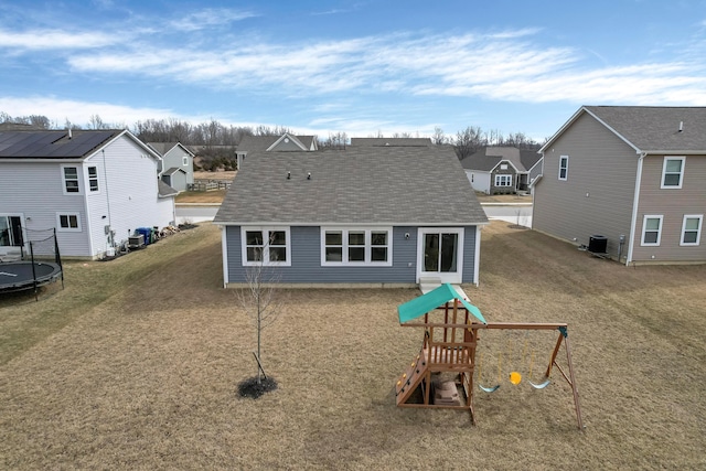 back of house featuring a playground, cooling unit, a shingled roof, a residential view, and a trampoline