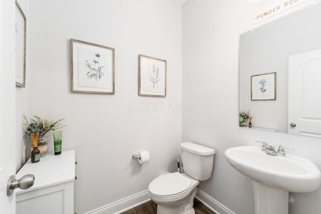 bathroom featuring toilet, baseboards, a sink, and wood finished floors