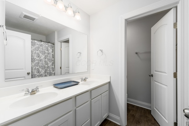 bathroom featuring wood finished floors, visible vents, a sink, and double vanity