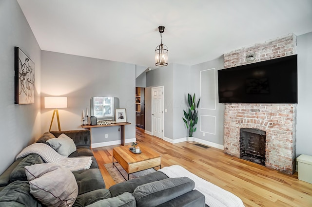 living room with visible vents, baseboards, wood finished floors, an inviting chandelier, and a brick fireplace