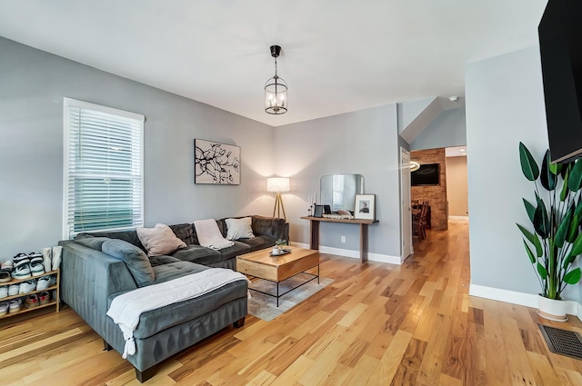 living room featuring a chandelier, light wood-type flooring, visible vents, and baseboards