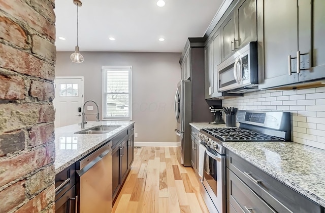 kitchen featuring tasteful backsplash, light wood-style flooring, appliances with stainless steel finishes, light stone countertops, and a sink