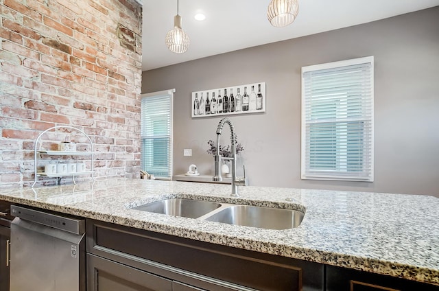 kitchen featuring brick wall, a sink, light stone countertops, dishwasher, and decorative light fixtures