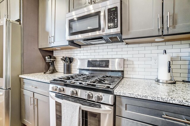 kitchen featuring gray cabinetry, stainless steel appliances, backsplash, and light stone countertops