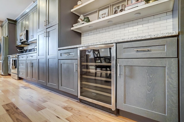 bar featuring stainless steel appliances, wine cooler, light wood-type flooring, and backsplash