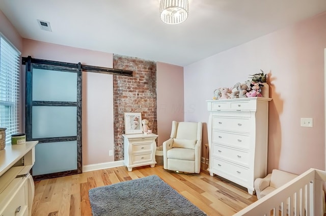 sitting room with a barn door, light wood-style flooring, visible vents, and baseboards