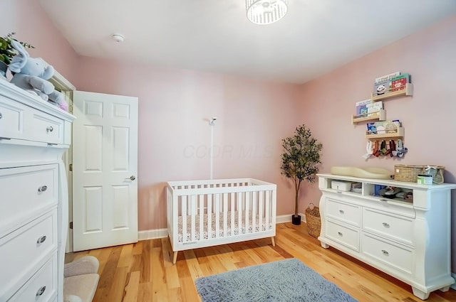 bedroom featuring light wood-style floors, a crib, and baseboards