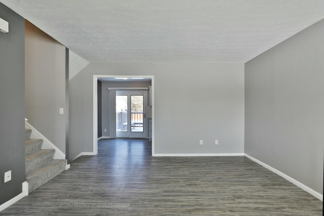 spare room featuring stairs, a textured ceiling, dark wood finished floors, and baseboards