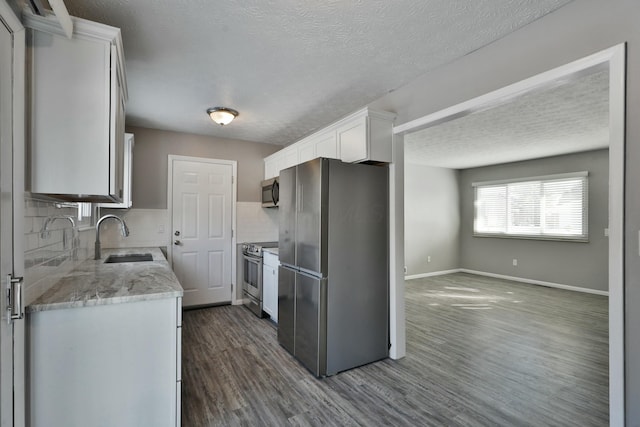 kitchen featuring decorative backsplash, appliances with stainless steel finishes, dark wood-type flooring, white cabinetry, and a sink