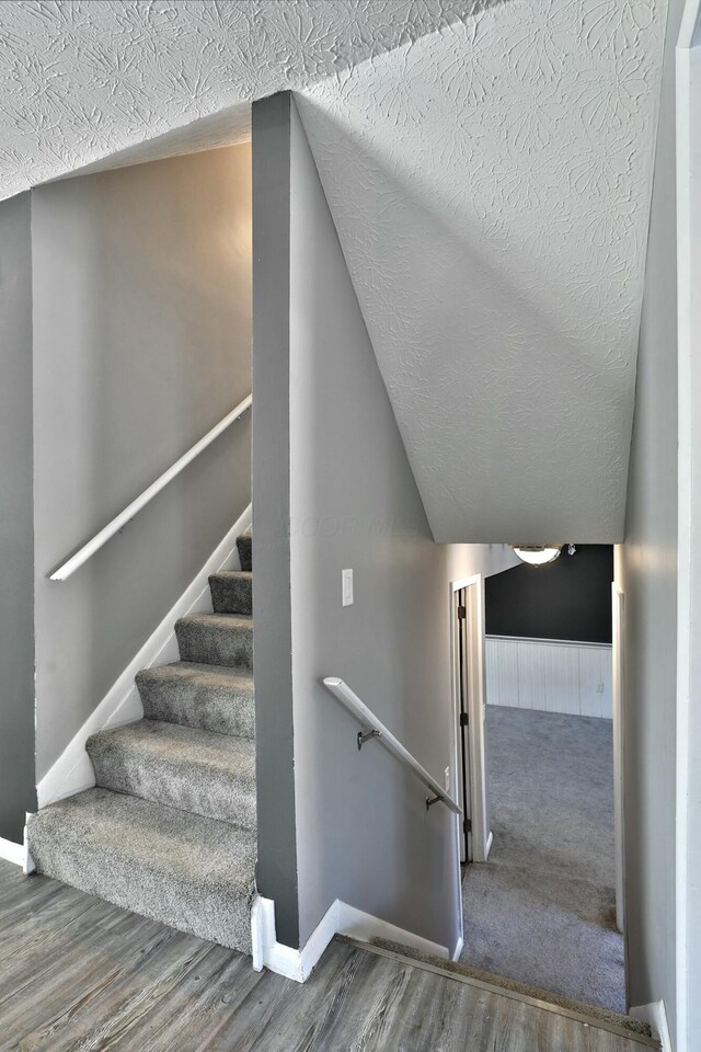 staircase with vaulted ceiling, a textured ceiling, baseboards, and wood finished floors