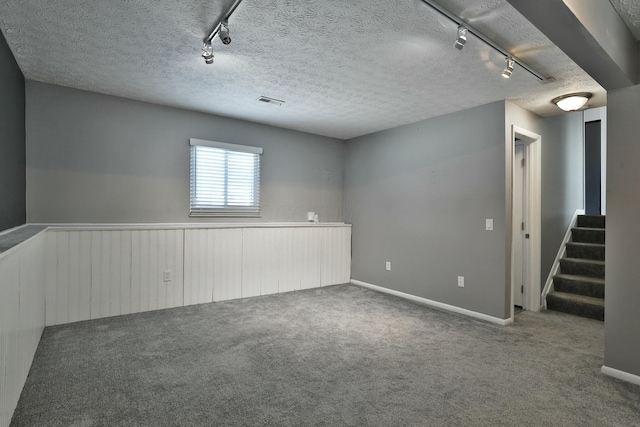 basement with carpet floors, track lighting, stairway, and a textured ceiling