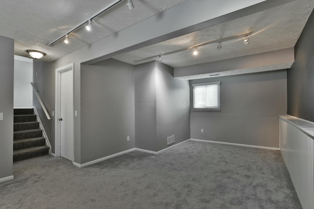 below grade area with visible vents, stairway, carpet flooring, a textured ceiling, and baseboards