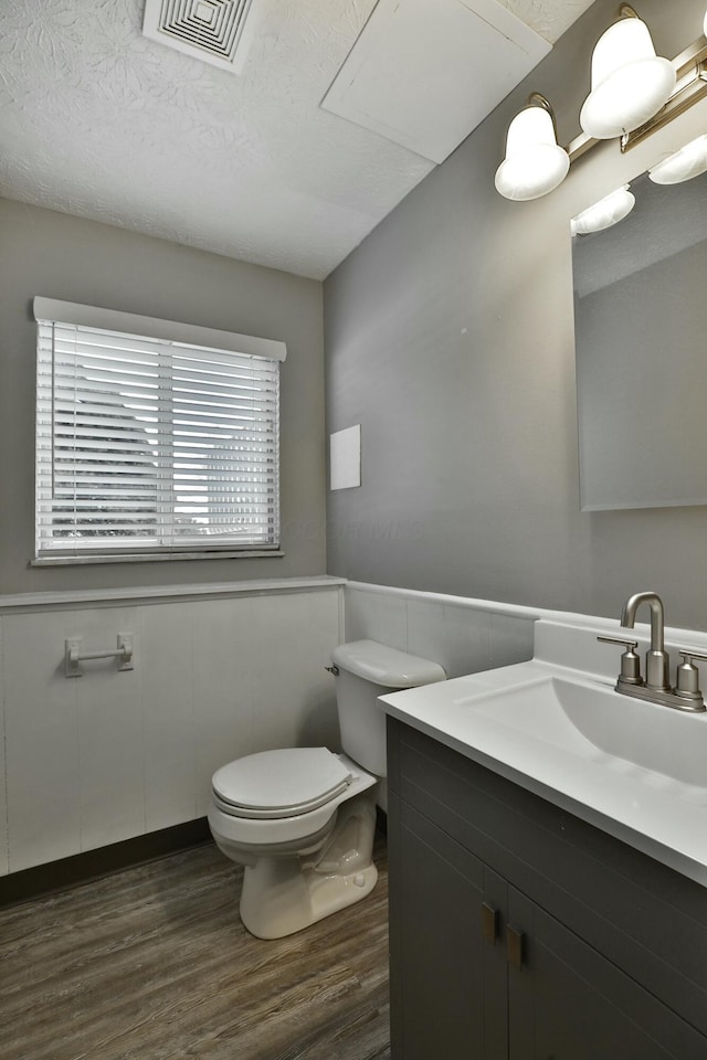 half bathroom featuring a wainscoted wall, visible vents, toilet, and wood finished floors