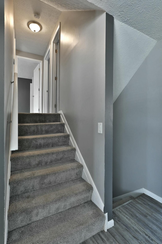 staircase with a textured ceiling, wood finished floors, and baseboards