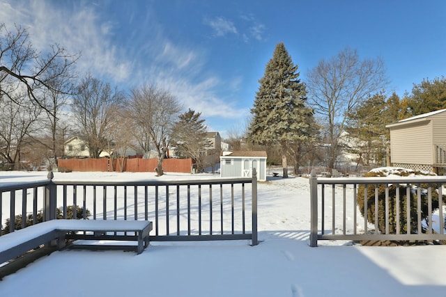 snow covered deck featuring a storage shed, an outdoor structure, and fence