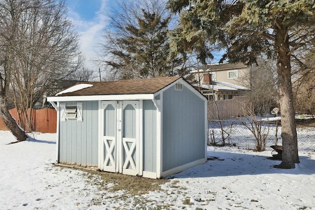 snow covered structure with an outbuilding, fence, and a storage unit