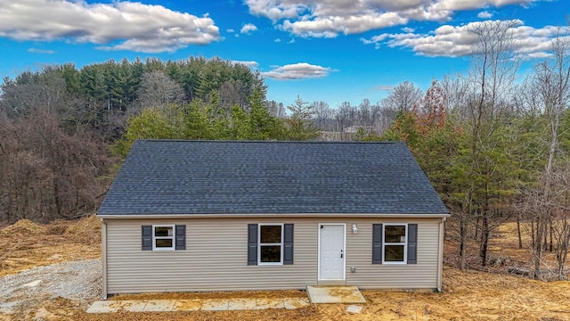 view of front of house with a shingled roof and a view of trees