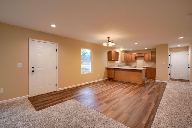 kitchen featuring a peninsula, baseboards, open floor plan, light countertops, and brown cabinetry