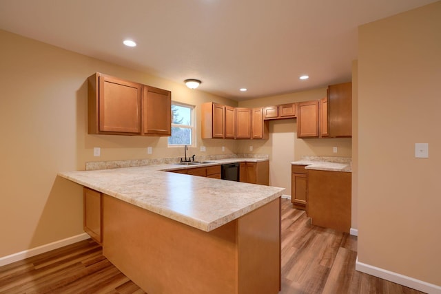 kitchen with light wood-type flooring, a sink, a peninsula, and baseboards