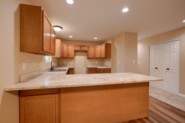 kitchen with recessed lighting, light countertops, a sink, wood finished floors, and a peninsula