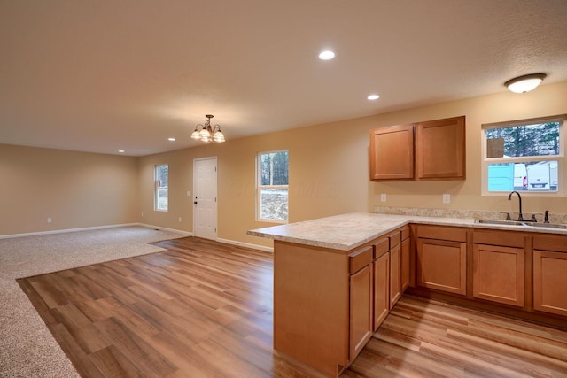 kitchen with light countertops, open floor plan, a sink, a peninsula, and baseboards