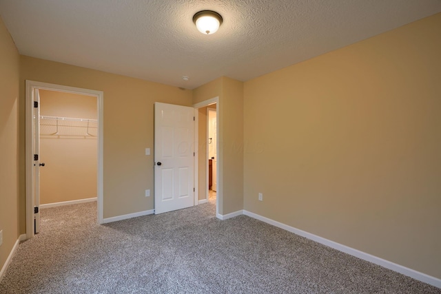 unfurnished bedroom with a textured ceiling, baseboards, a closet, carpet, and a walk in closet