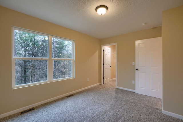 carpeted spare room with visible vents, a textured ceiling, and baseboards