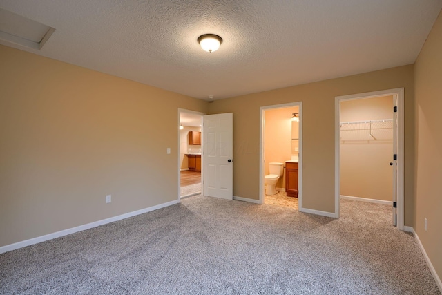 unfurnished bedroom with light carpet, a spacious closet, baseboards, and connected bathroom