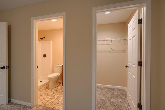 bathroom with a stall shower, a walk in closet, baseboards, and toilet