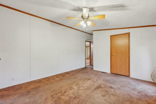 carpeted spare room featuring a ceiling fan, a textured ceiling, visible vents, and crown molding