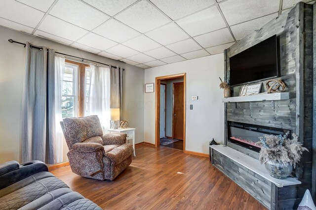 living area with a large fireplace, wood finished floors, a paneled ceiling, and baseboards