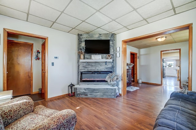 living room featuring a large fireplace, wood finished floors, a paneled ceiling, and baseboards