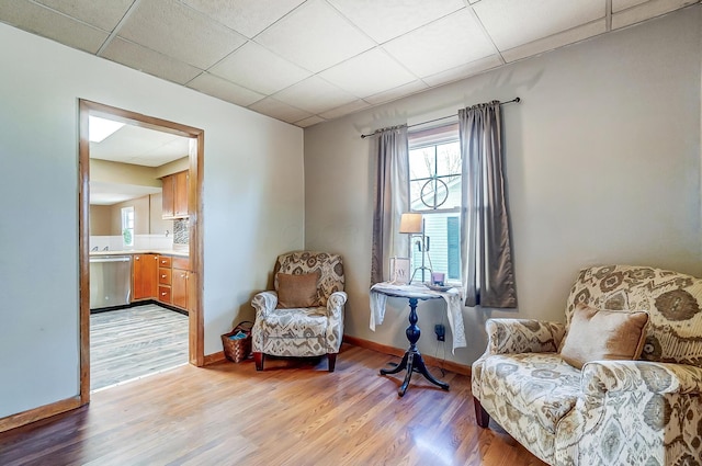 sitting room with light wood finished floors, a drop ceiling, and baseboards