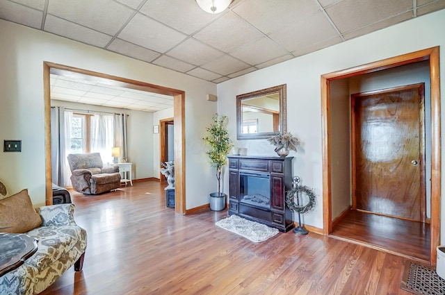 living room with a drop ceiling, wood finished floors, and baseboards