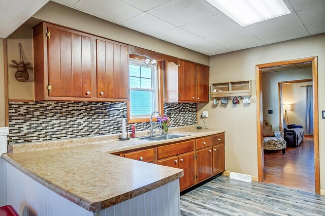 kitchen featuring brown cabinets, backsplash, light wood-style floors, a sink, and a peninsula