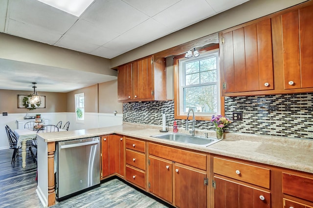 kitchen featuring a peninsula, stainless steel dishwasher, a sink, and light countertops