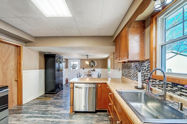 kitchen featuring brown cabinetry, dishwasher, a wainscoted wall, a peninsula, and a sink