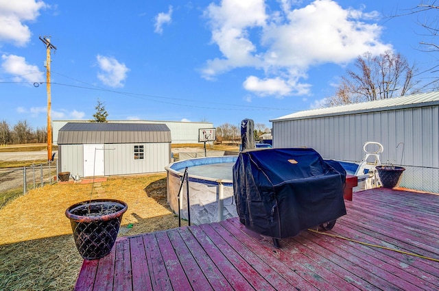 wooden deck with an outdoor pool, an outbuilding, a grill, a storage unit, and fence