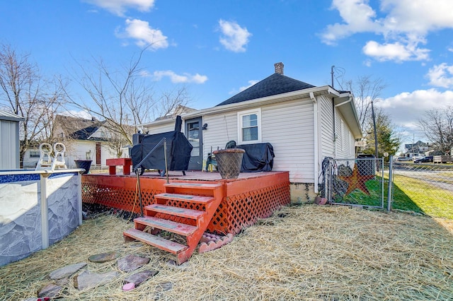 back of house with a chimney, a gate, fence, a wooden deck, and a pool