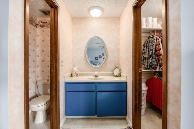 full bathroom featuring visible vents, toilet, a textured ceiling, vanity, and wallpapered walls