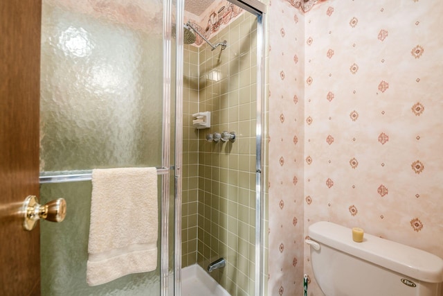 bathroom featuring toilet, wallpapered walls, and a tile shower