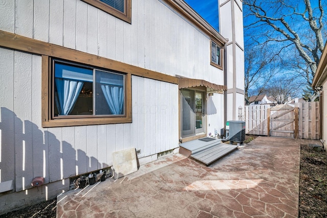 view of home's exterior with a chimney, a gate, a patio area, central AC, and fence