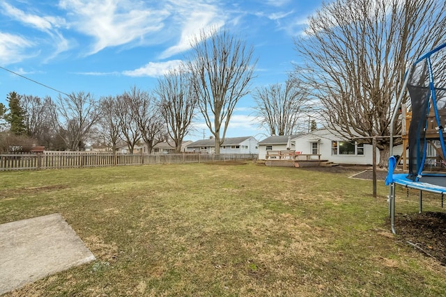 view of yard with a trampoline, a deck, and a fenced backyard