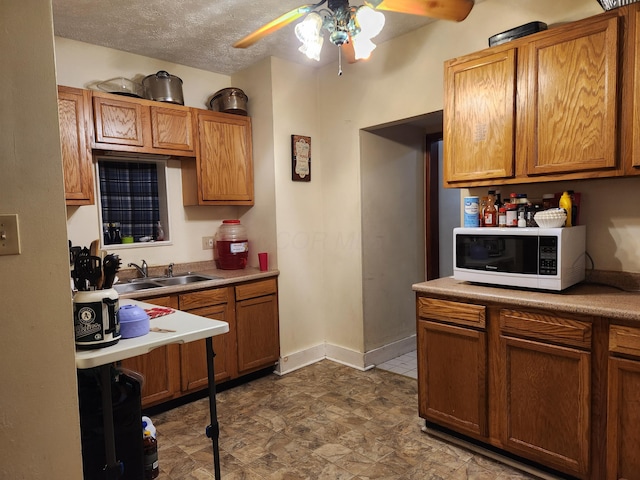 kitchen featuring brown cabinetry, a ceiling fan, white microwave, a textured ceiling, and a sink