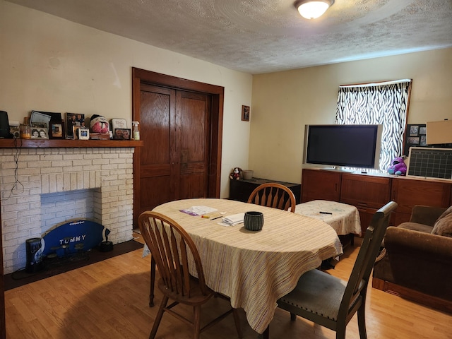 dining room featuring a brick fireplace, a textured ceiling, and wood finished floors