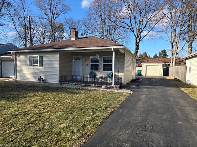 view of front of house with a chimney, a porch, aphalt driveway, an outbuilding, and a front lawn