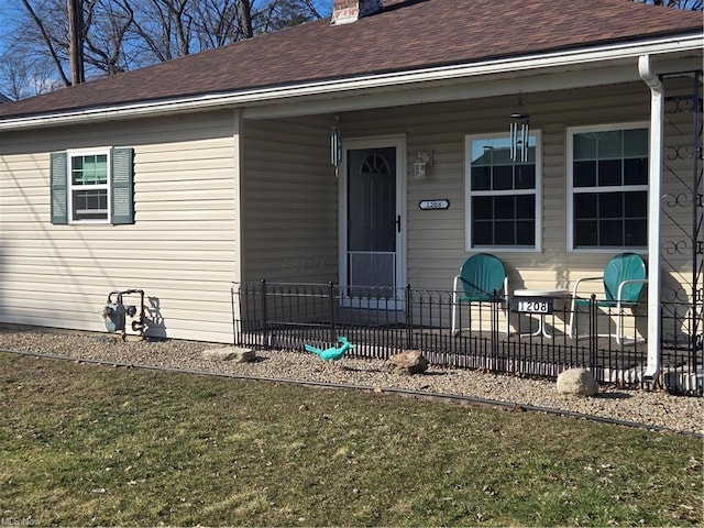 view of exterior entry with covered porch, a shingled roof, a chimney, and fence