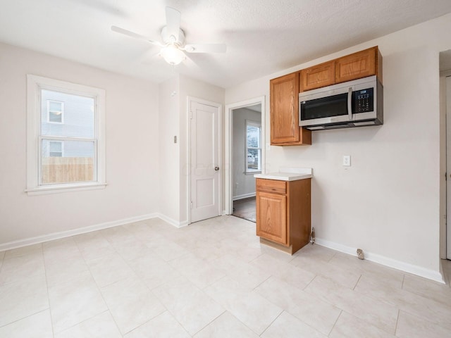 kitchen with brown cabinets, stainless steel microwave, baseboards, and a ceiling fan