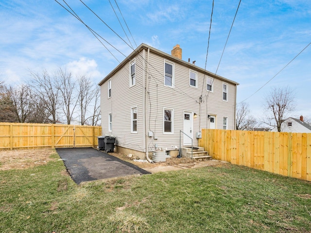 rear view of house with central AC unit, a chimney, a gate, fence, and a yard